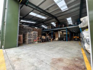 Inside a wood furnishings storage building with a mezzanine floor in the background and lots of pallets and storage bags
